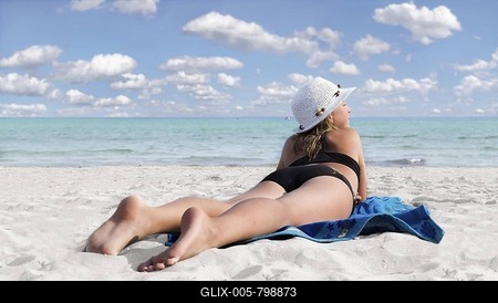 Girl with hat on a white sandy beach with turquoise sea lying on a blue towel-stock-foto