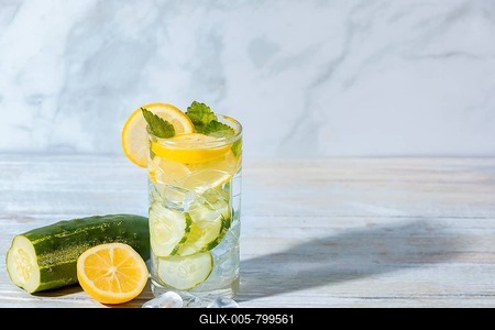 A glass of cucumber water with lemon slices, mint leaves and ice cube cubes, cucumber and lemon on a table next to it-stock-foto