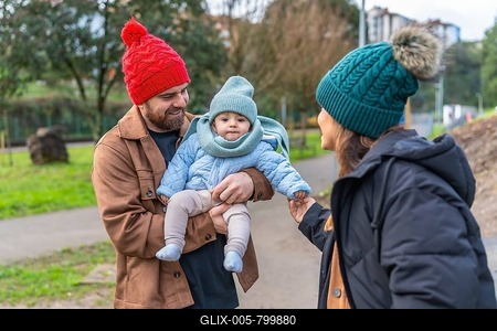 Parents holding their baby while enjoying a winter day outdoors in a park, wearing warm clothes and woolen hats-stock-foto