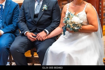 Bride and groom holding hands, sitting on wooden chairs, during wedding ceremony, with bouquet in bride's hand-stock-foto