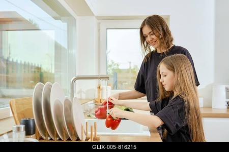 A mother watches her daughter wash vegetables under running water in the kitchen-stock-foto