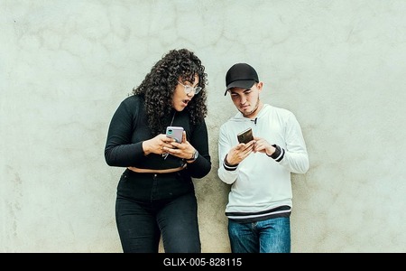 Two teenagers together checking their cell phones, Two smiling friends checking their cell phones, Two teenage friends checking their cell phones and smiling, Guy and girl leaning on a wall checking their cell phones-stock-foto