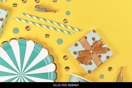 Teal blue paper plates, gift box, small golden Champagne bottles and confetti on yellow background-stock-foto