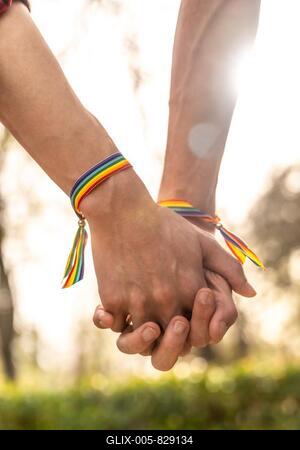 Vertical close-up of a gay men with rainbow bracelets holding hands-stock-foto