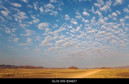 Gravel road on arid plain, isolated mountain ridges, fluffy clouds at edge of Namib Desert, evening light, Kulala Wilderness Reserve, Namibia-stock-foto