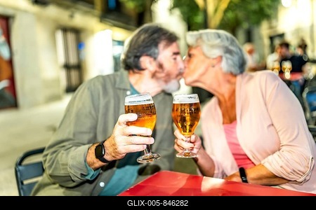 Senior couple kissing while toasting with beer in an outdoor terrace in the city-stock-foto