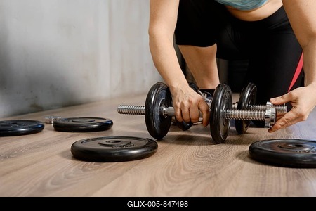 A person is adjusting weights on a dumbbell while preparing for an intense workout. The setting is a well-lit fitness center, with various weights scattered on the floor-stock-foto