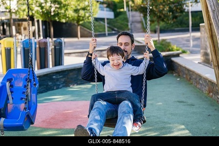 A father and his son with Down syndrome share a joyful moment on a swing in a sunny park. The child laughs gleefully, capturing the essence of pure happiness and family bonding-stock-foto