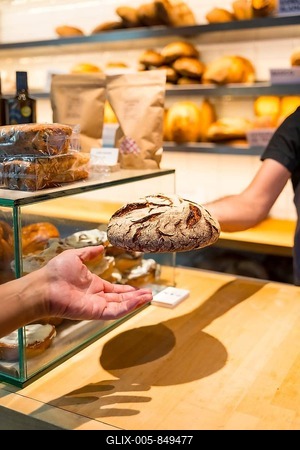 Hands of customer in the bakery shop buying an artisan bread from the baker in the workshop, vertical photo-stock-foto