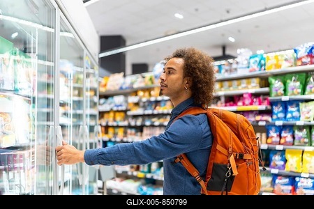 Young african american man with curly hair and a backpack opening a supermarket freezer, thoughtfully choosing frozen food while shopping in a modern grocery aisle-stock-foto