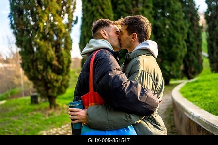 Two men are kissing in a park, embracing each other tenderly, showcasing their love and commitment-stock-foto