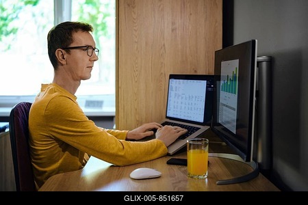 A middle-aged man focused on his work sits at a wooden desk with two computer screens. He enters various data and looks at the chart, analyzing and predicting various scenarios-stock-foto
