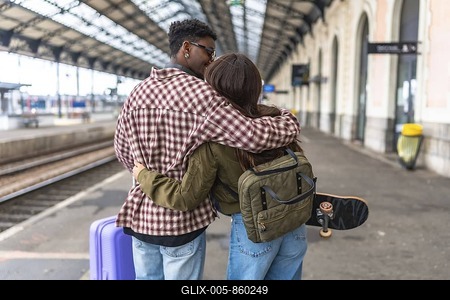 Young couple kissing and hugging on a train station platform, ready for their journey, with luggage and skateboard-stock-foto