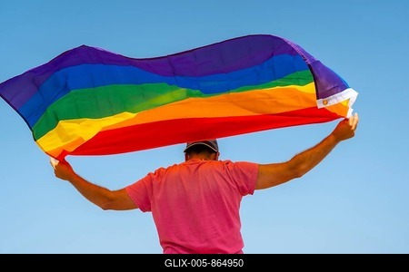 A gay person with the LGBT flag on his back moving with the wind with the sky in the background, symbol of homosexuality, rainbow flag-stock-foto