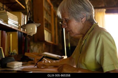 Serious mature woman in glasses thoughtful focused senior writing a letter at home-stock-foto