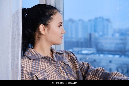 Dreamy young woman in warm shirt and socks sitting on windowsill and looking to the window-stock-foto