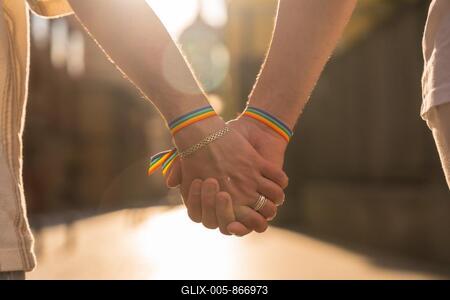 Detail of the holding hands of a couple of homosexual men with the rainbow flag at the pride party in the city at sunset, lgbt concept-stock-foto