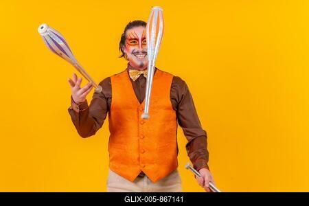 Happy juggler man in makeup vest juggling maces on a yellow background-stock-foto