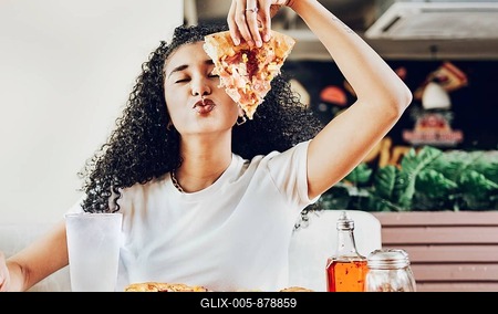 Girl in a restaurant showing slice of pizza giving a kiss to the camera. Beautiful curly haired woman showing slice of pizza in a restaurant with copy space-stock-foto