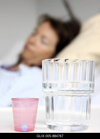 Patient in a hospital bed, medicine and a glass of water on the bedside table, hospital-stock-foto