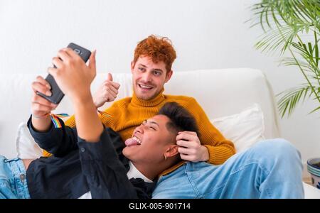 Beautiful gay couple being romantic indoors on the sofa, gay couple, taking a selfie-stock-foto