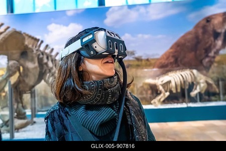 Woman experiencing virtual reality with a headset on, exploring ancient animals and paleontology in a modern museum exhibition, blending technology with education-stock-foto