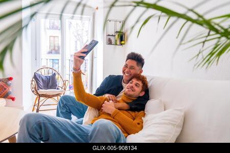 Beautiful gay couple being romantic indoors at home on the sofa, taking a selfie, lgbt concept-stock-foto