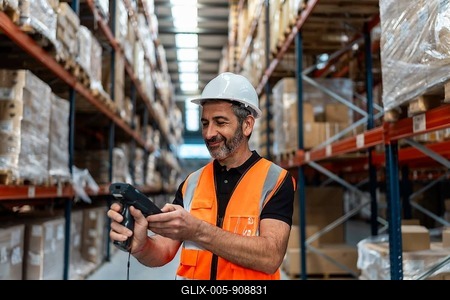 Male logistics worker wearing a hard hat and safety vest, scanning packages on shelves in a large distribution warehouse, managing stock and supply chain operations-stock-foto