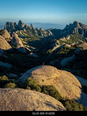 A breathtaking view of Montserrat's rugged rock formations in Catalonia, Spain. The image captures a lone figure standing on a large boulder, surrounded by lush greenery-stock-foto