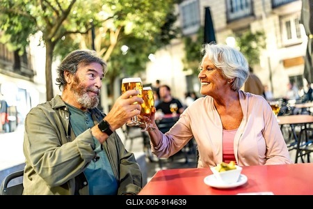 Happy relaxed senior couple toasting with beer in sidewalk cafeteria at night-stock-foto