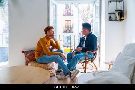 Beautiful gay couple being romantic at home by the balcony of home talking, lgbt concept-stock-foto