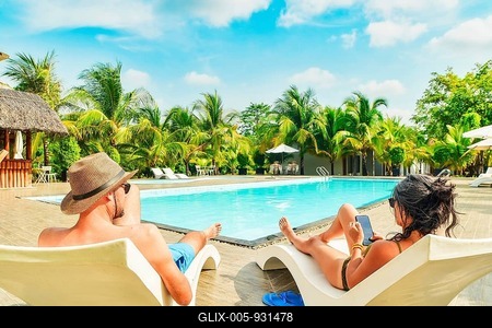 Couple lay on sunbeds enjoy sunbathing relax scroll phone internet on all-inclusive vacation holidays at tropical resort with swimming pool surrounded by coconut palm trees on sunny hot tropical day-stock-foto