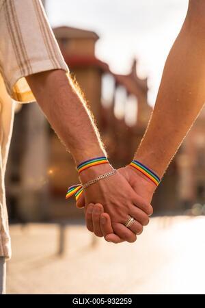 Detail of the holding hands of a couple of homosexual men with the rainbow flag at the pride party in the city at sunset, lgbt concept-stock-foto