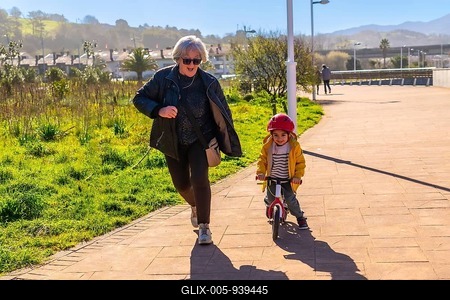 Grandmother jogging behind her grandson riding a balance bike in a park, having fun together on a sunny day-stock-foto