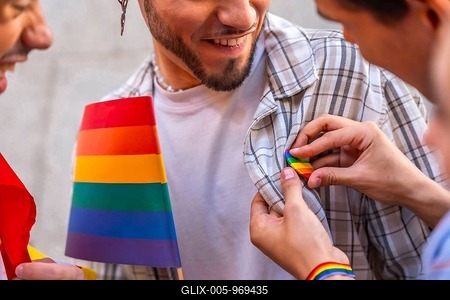 Happy man smiles as someone pins a rainbow flag badge to his plaid shirt, celebrating lgbtq pride, support, diversity and unity at an outdoor event or parade-stock-foto