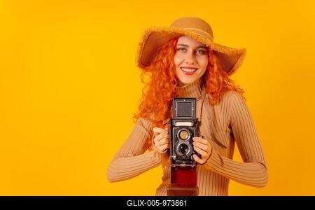 Red-haired woman tourist on a yellow background, studio shot, with a vintage photography camera-stock-foto