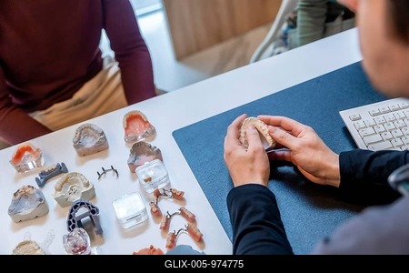 Dentist explaining to patient treatment with dental prosthesis, surrounded by various dental models in clinic-stock-foto