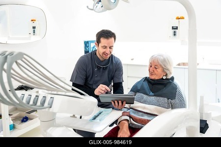 Dentist showing information on digital tablet to a senior patient during a consultation in a modern dental clinic, discussing treatment options and healthcare-stock-foto