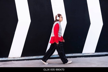 Latina woman in a vibrant red shirt and headphones walks confidently against a bold black and white mural backdrop The stylish urban scene captures youthful energy and diversity-stock-foto