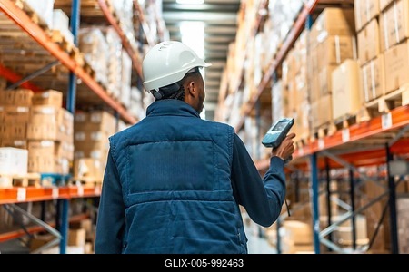 Rear view of an african worker with waistcoat and helmet scanning packages with wireless scanner in a distribution warehouse-stock-foto