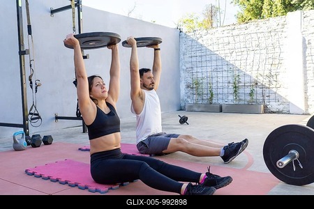 Young hispanic man and woman lifting weights while sitting on mats in a backyard gym, embracing a healthy lifestyle together and enjoying their workout in the summer sunlight-stock-foto