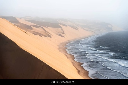 Sand dunes with wave patterns and sea in evening light, wind blowing sand across the dunes, Atlantic coast and sandy desert with sea of dunes, impressive desert landscape, Sandwich Harbour, Namib Naukluft Park, Namib Desert, Namibia-stock-foto