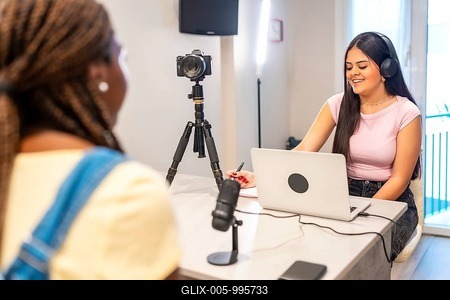 Two teenage girls creating digital content with laptop, camera, microphone, and headphones, enjoying their shared activity-stock-foto