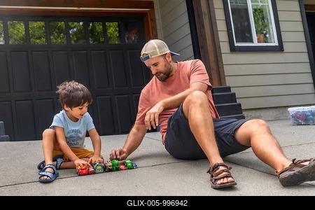 Father and son are sitting on the ground in their driveway, playing with a collection of toy cars, enjoying quality time together on a sunny day-stock-foto