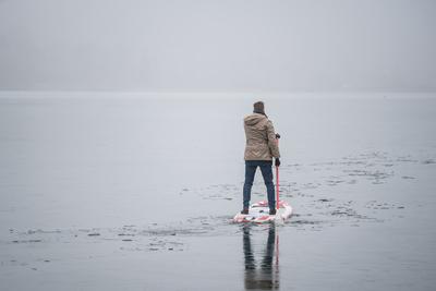 Man standing on stand up paddleboard on icy lake-stock-foto