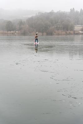 Man standing on stand up paddleboard on icy lake-stock-foto