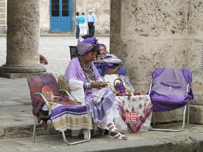 Havana, 25 January 2015Cuban woman in purple selling trinkets. Csecsebecs?it ?rus?t? kubai asszony lila d?szruh?ban a Katedr?lis t?r ?rk?dja alatt. T?bl?j?n spnyol felirat: ker?ljenek a hamisak!-stock-foto