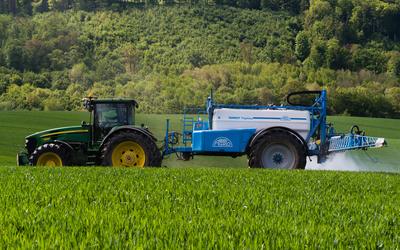 A farmer spraying on the spring wheat field with a John Deere tractor and a mamut topline sprayer.-stock-photo