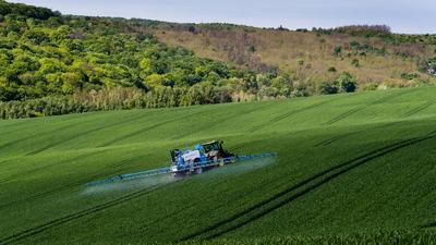 A farmer spraying on the spring wheat field with a John Deere tractor and a mamut topline sprayer.-stock-photo