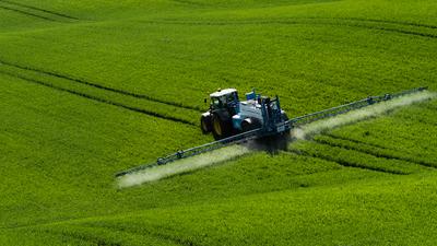 A farmer spraying on the spring wheat field with a John Deere tractor and a mamut topline sprayer.-stock-photo